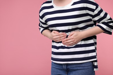 Young woman suffering from stomach pain on pink background, closeup. Space for text