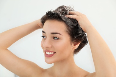 Photo of Woman applying shampoo onto her hair against light background