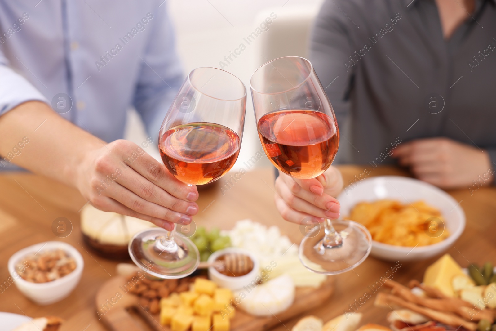 Photo of People clinking glasses with rose wine above wooden table indoors, closeup