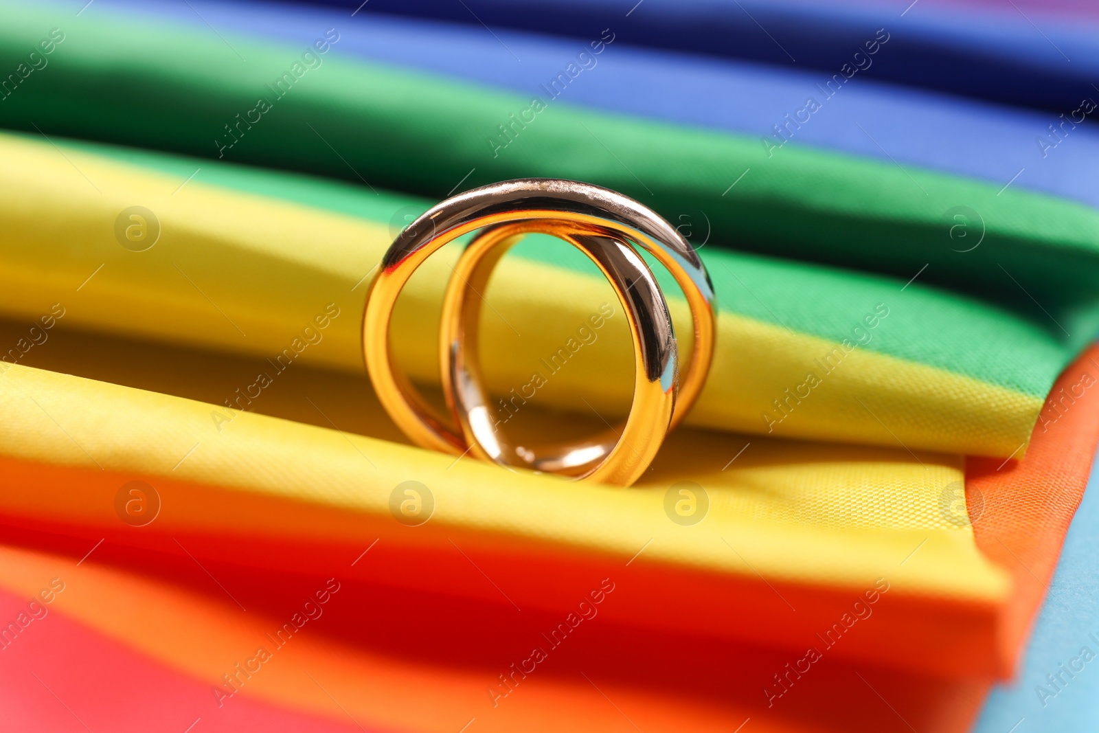 Photo of Rainbow LGBT flag and wedding rings on light blue background, closeup