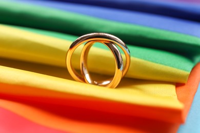 Photo of Rainbow LGBT flag and wedding rings on light blue background, closeup