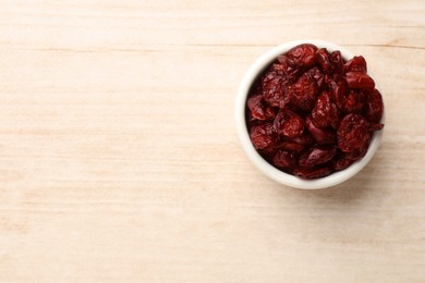 Photo of Dried cranberries in bowl on wooden table, top view