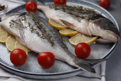 Photo of Raw dorado fish with thyme, lemon slices and tomatoes on table, closeup