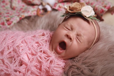 Photo of Cute newborn baby girl with floral headband lying on fuzzy rug, closeup