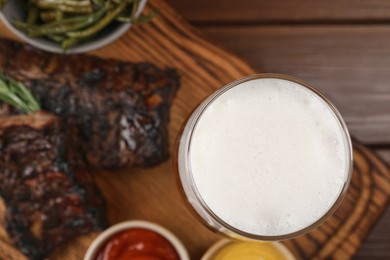 Photo of Glass of beer, delicious grilled ribs and sauces on wooden table, closeup. Space for text