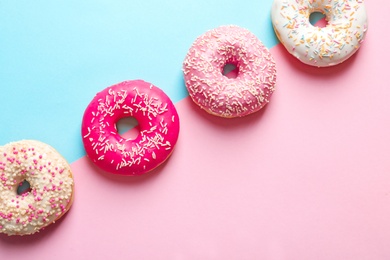 Delicious doughnuts with sprinkles on color background, top view