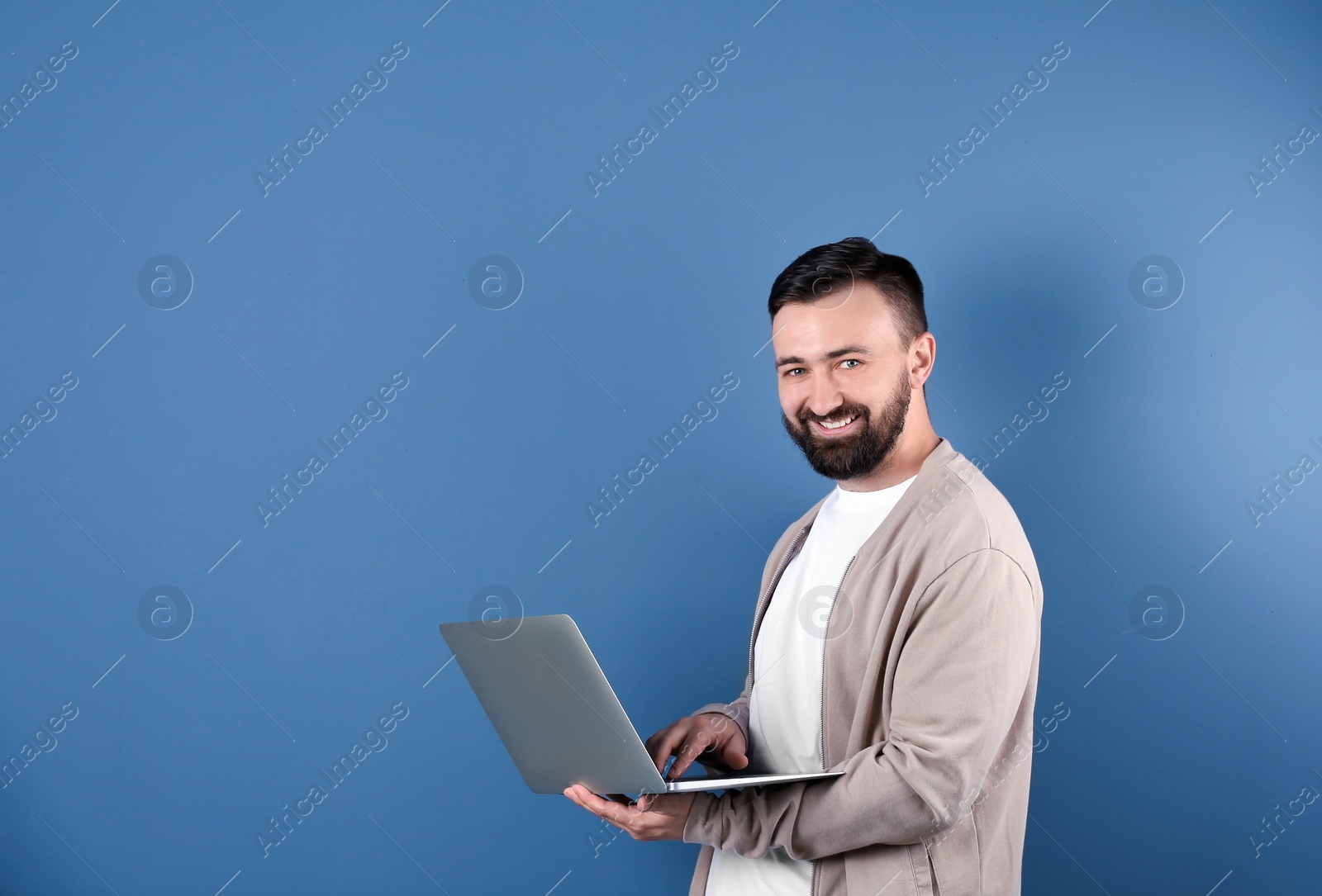 Photo of Portrait of handsome bearded man with laptop on color background