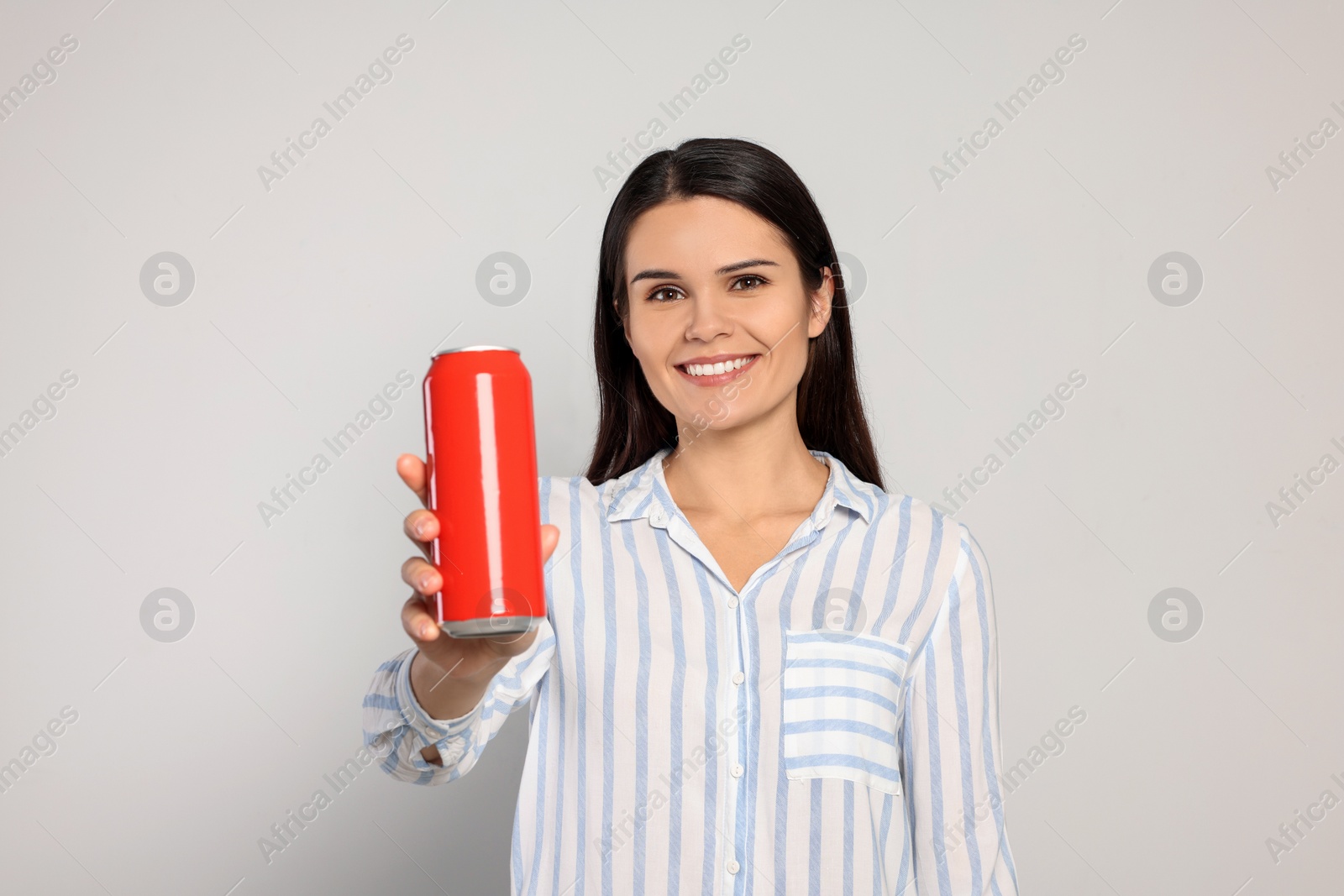 Photo of Beautiful young woman holding tin can with beverage on light grey background