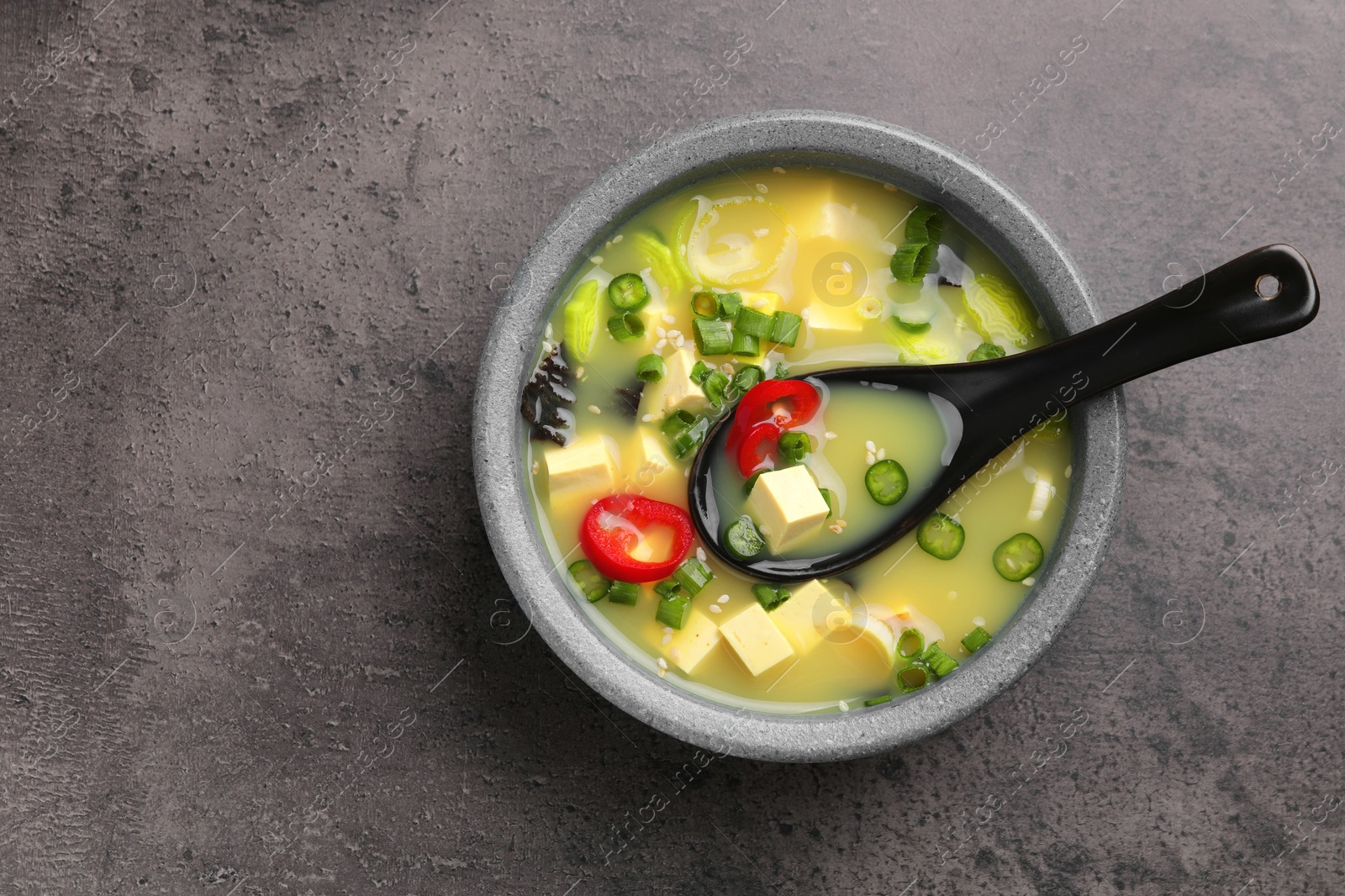 Photo of Bowl of delicious miso soup with tofu and spoon on grey table, top view. Space for text