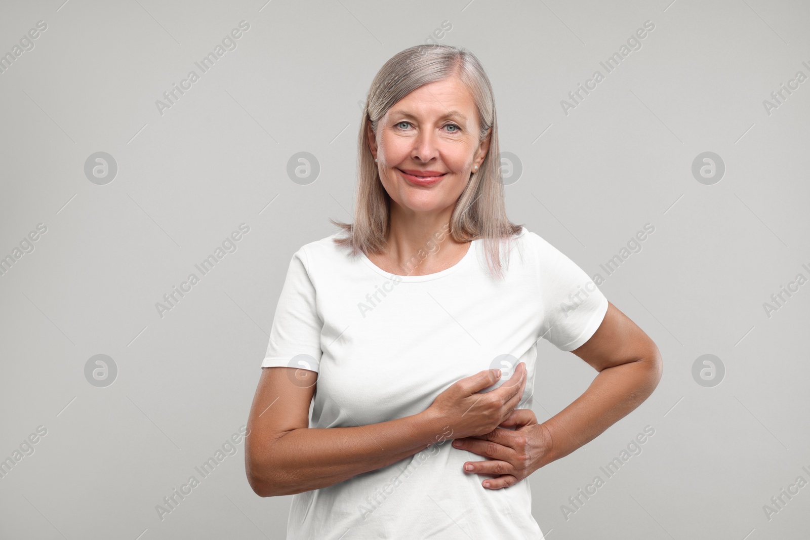 Photo of Beautiful senior woman doing breast self-examination on light grey background