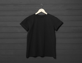 Hanger with stylish black T-shirt on gray wooden wall