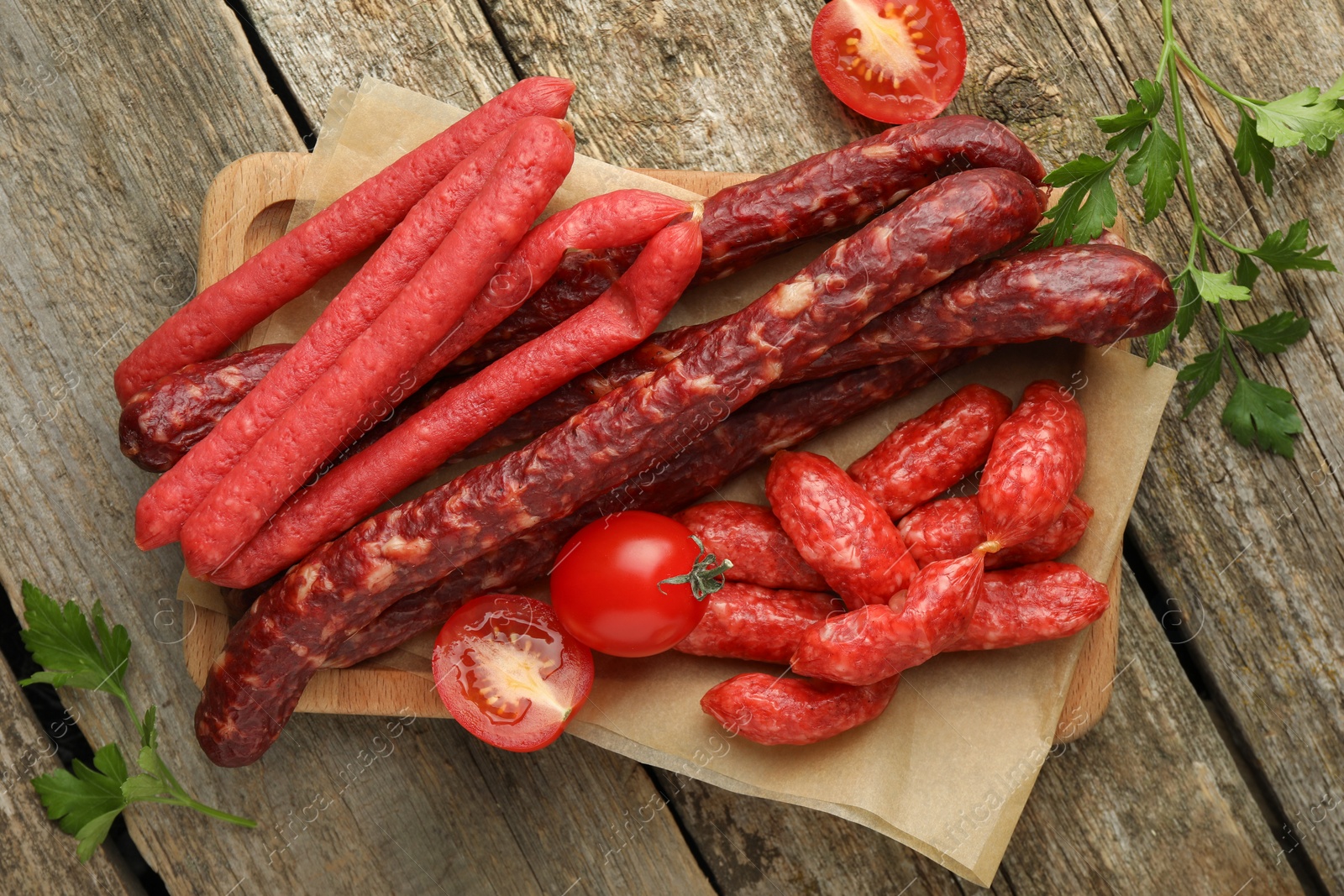 Photo of Thin dry smoked sausages, tomatoes and parsley on old wooden table, flat lay