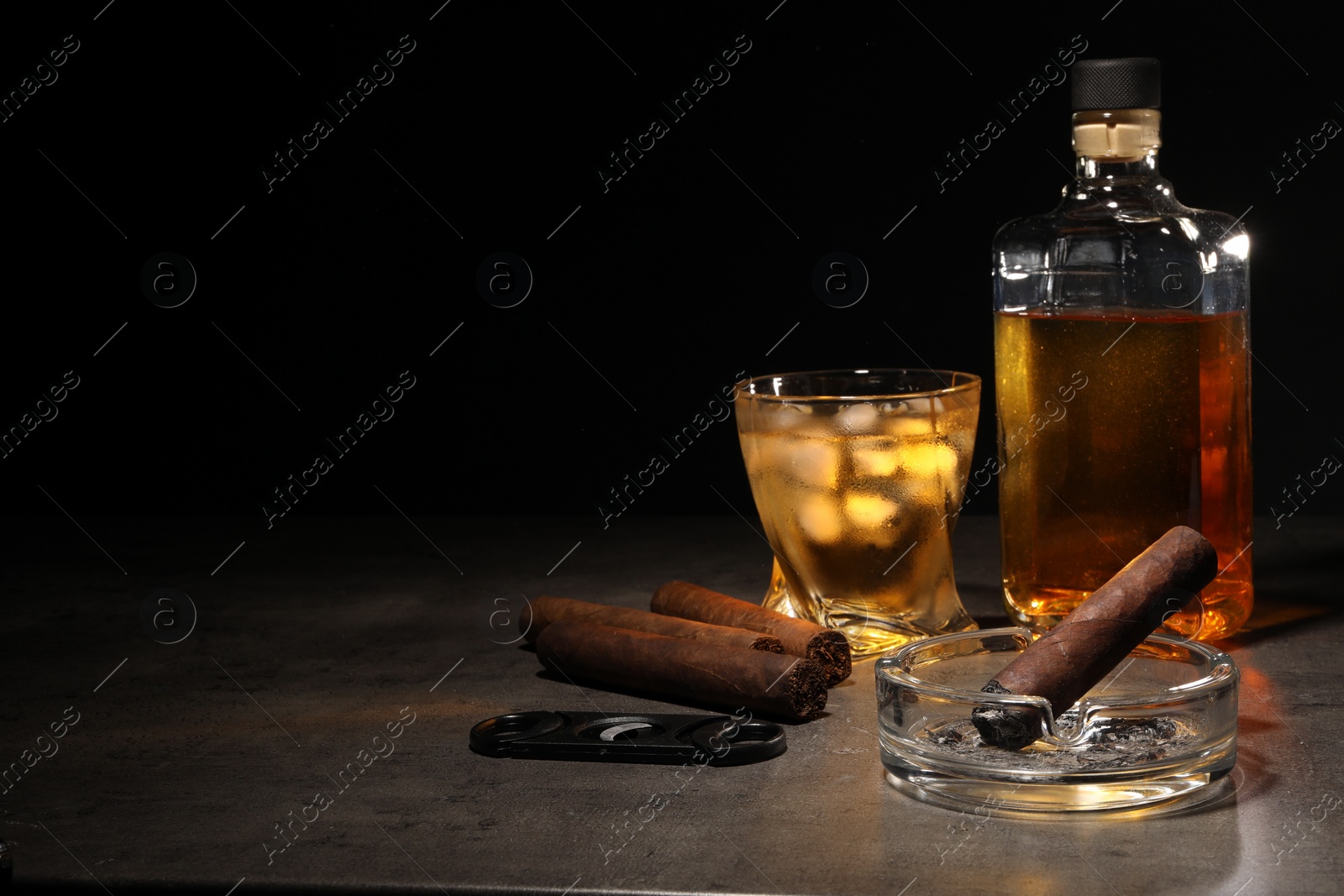 Photo of Cigars, ashtray, whiskey and cutter on grey table against black background. Space for text