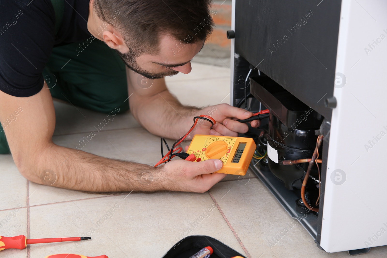 Photo of Male technician in uniform repairing refrigerator indoors