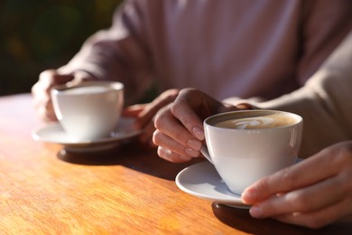 Photo of Couple with cups of aromatic coffee at wooden table in cafe, closeup