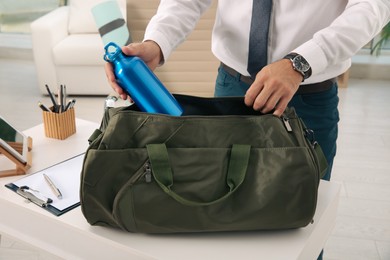 Photo of Businessman packing sports stuff for training into bag in office, closeup