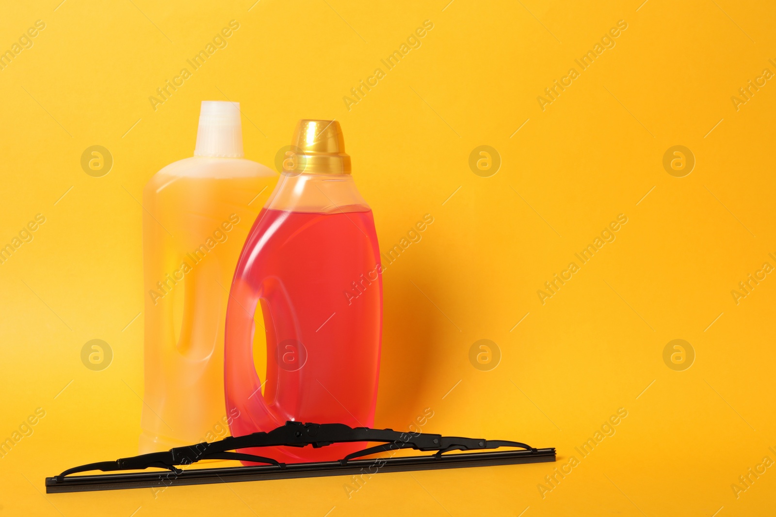 Photo of Bottles of windshield washer fluids and wiper on yellow background. Space for text