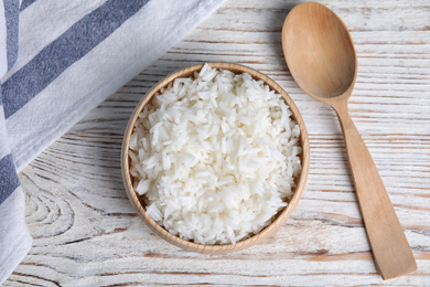 Photo of Bowl with tasty cooked rice on white wooden table, flat lay