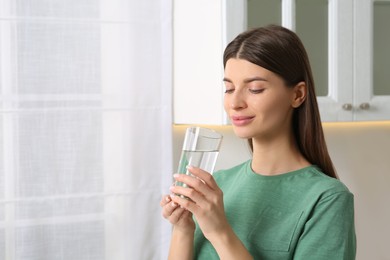 Healthy habit. Woman holding glass with fresh water indoors. Space for text