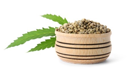 Bowl of hemp seeds with green leaf on white background