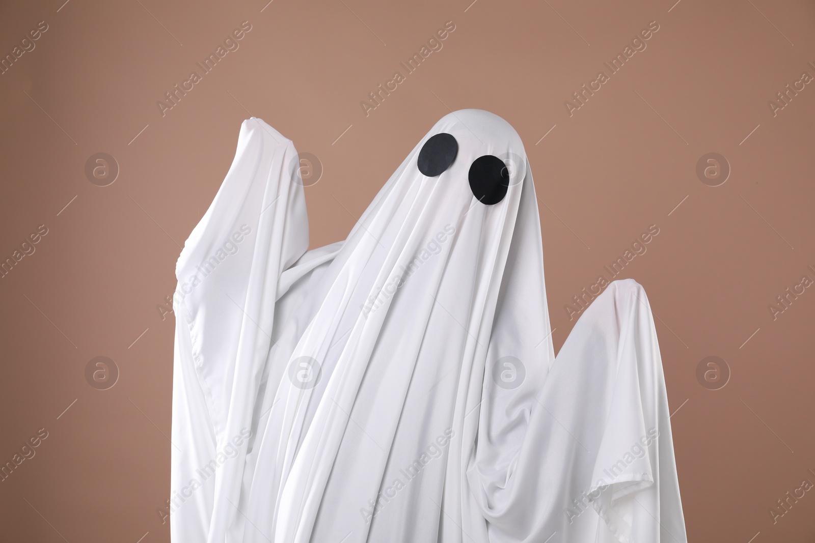 Photo of Creepy ghost. Person covered with white sheet on dark beige background