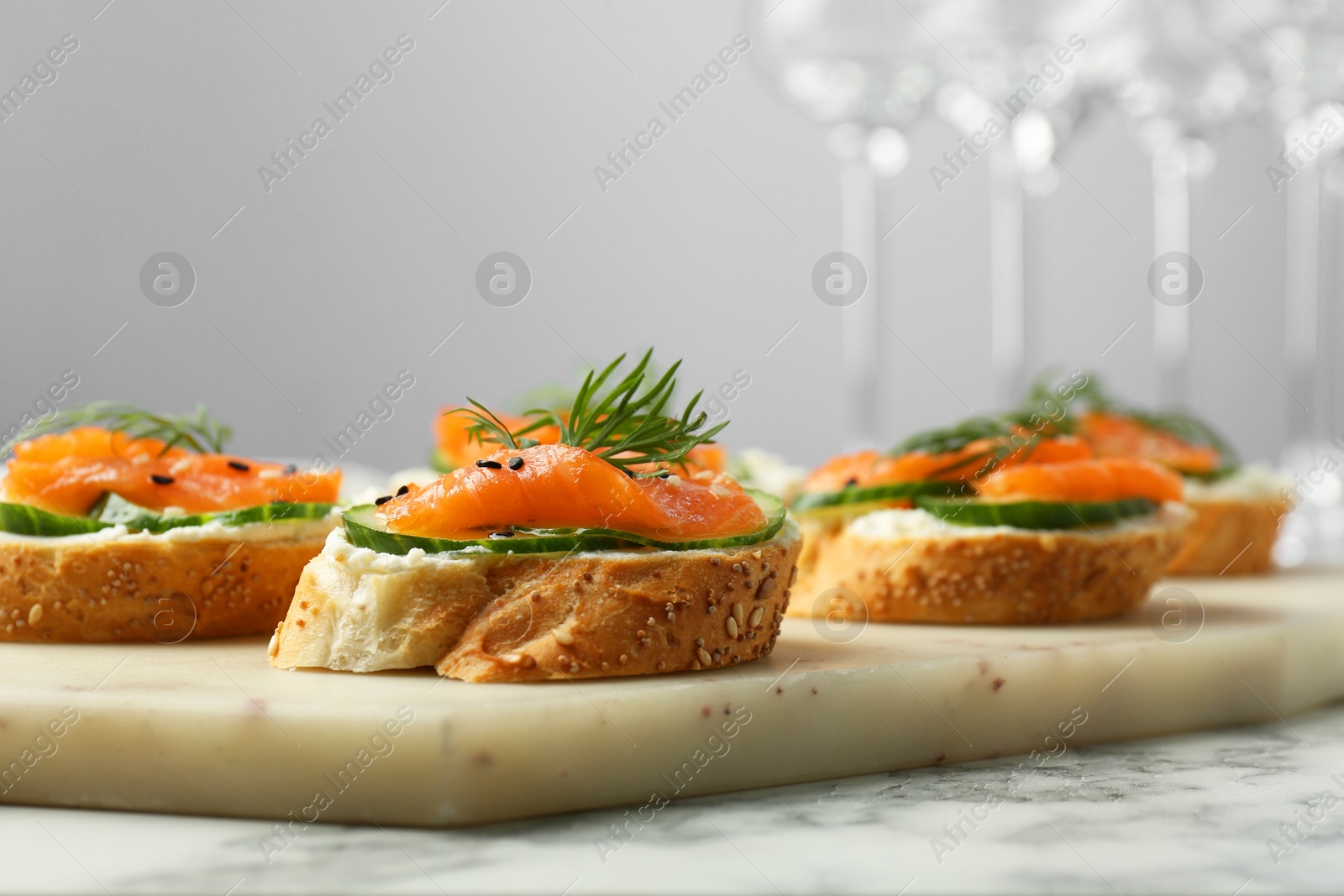 Photo of Tasty canapes with salmon, cucumber and cream cheese on white marble table, closeup