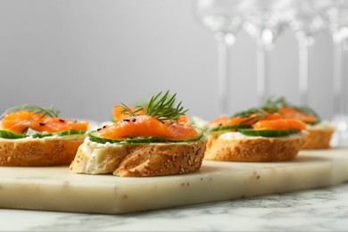 Tasty canapes with salmon, cucumber and cream cheese on white marble table, closeup