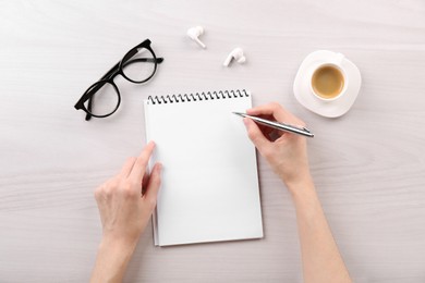 Woman with notebook and pen at white wooden table, top view. Space for text