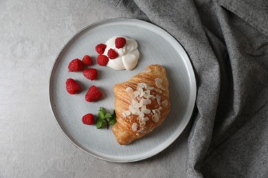 Photo of Delicious croissant with raspberries, cream and almond flakes on grey table, top view
