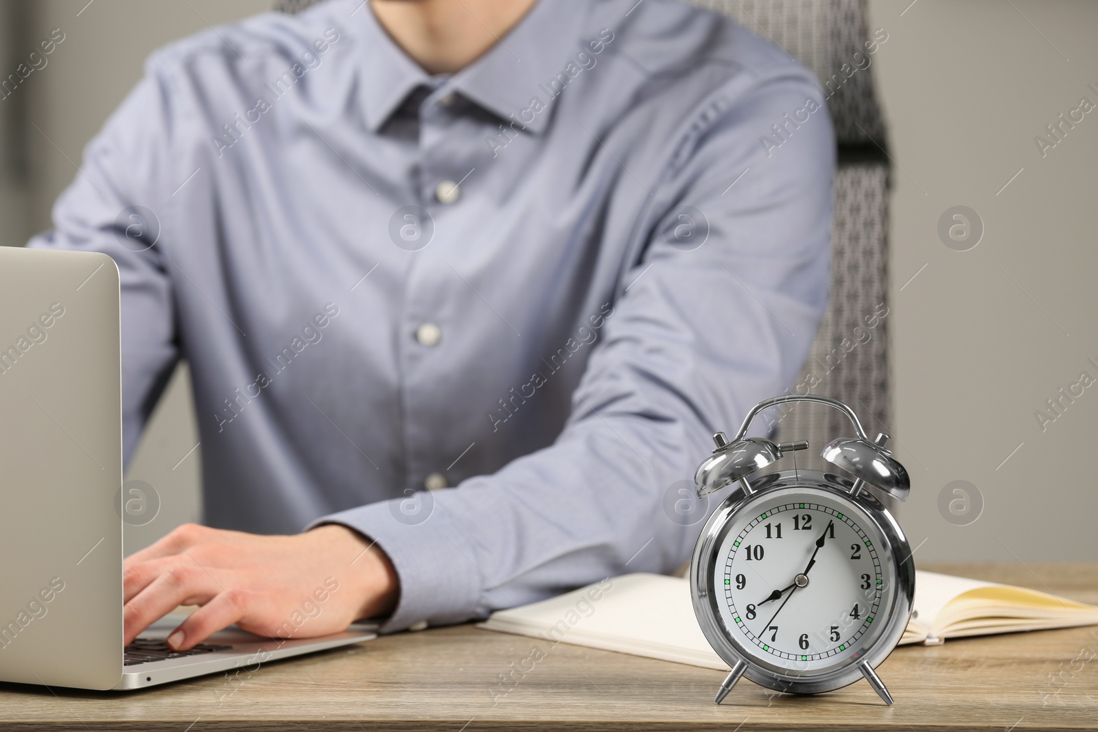 Photo of Silver alarm clock and man working at wooden table, closeup