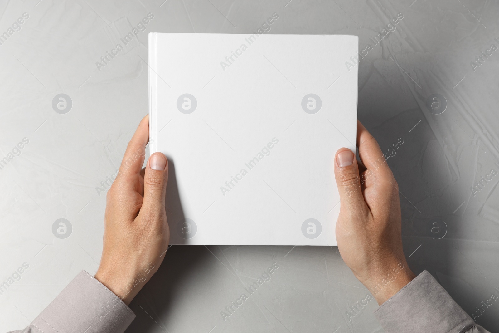 Photo of Man holding blank book at light grey table, top view. Mockup for design