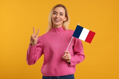 Image of Happy young woman with flag of France showing V-sign on yellow background