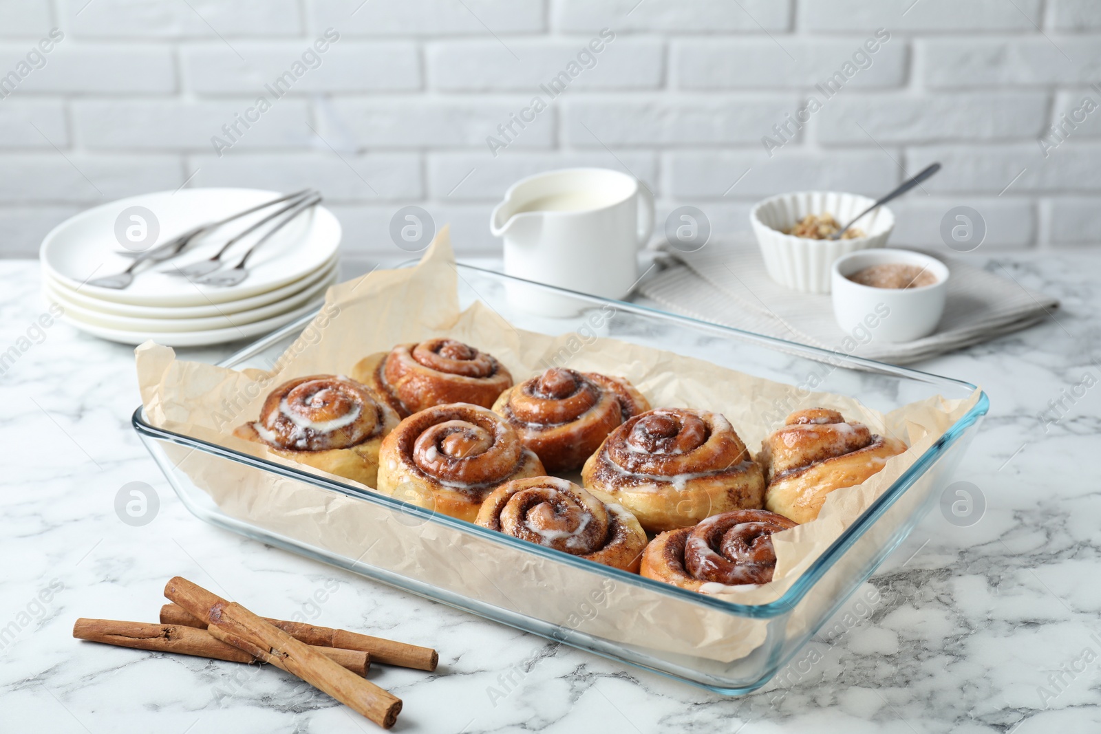 Photo of Baking dish with tasty cinnamon rolls and sticks on white marble table