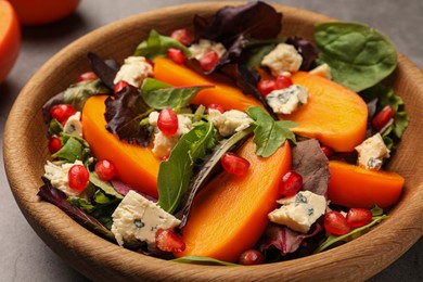 Photo of Delicious persimmon salad with cheese and pomegranate on grey table, closeup