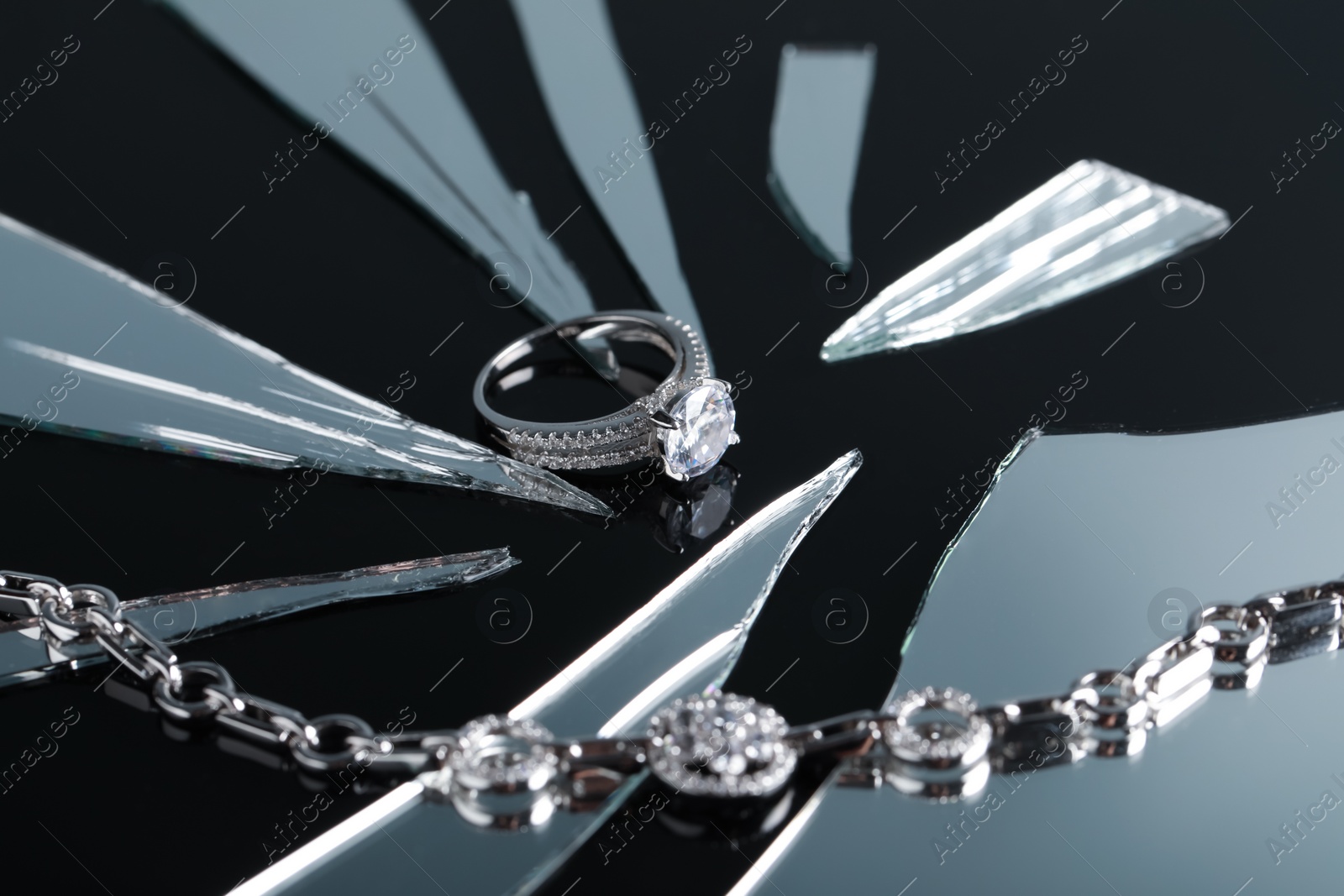 Photo of Luxury jewelry. Stylish presentation of elegant ring and bracelet on black mirror surface with broken glass, closeup
