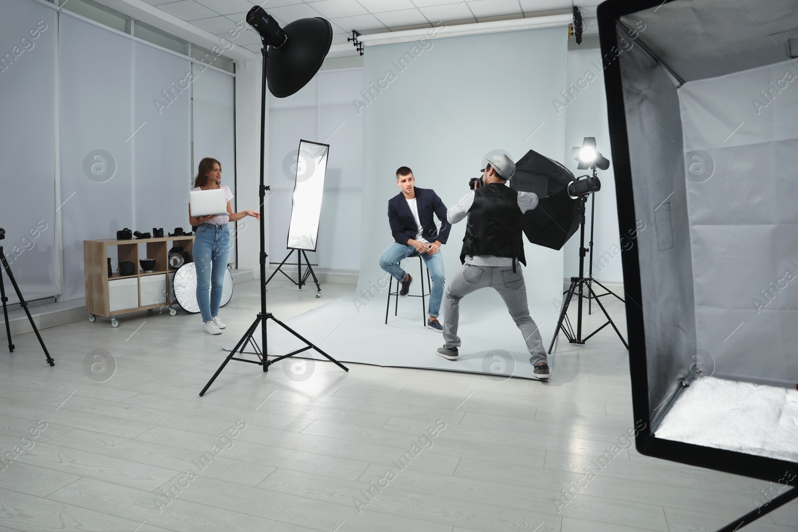 Photo of Professional photographer with assistant taking picture of young man in modern studio