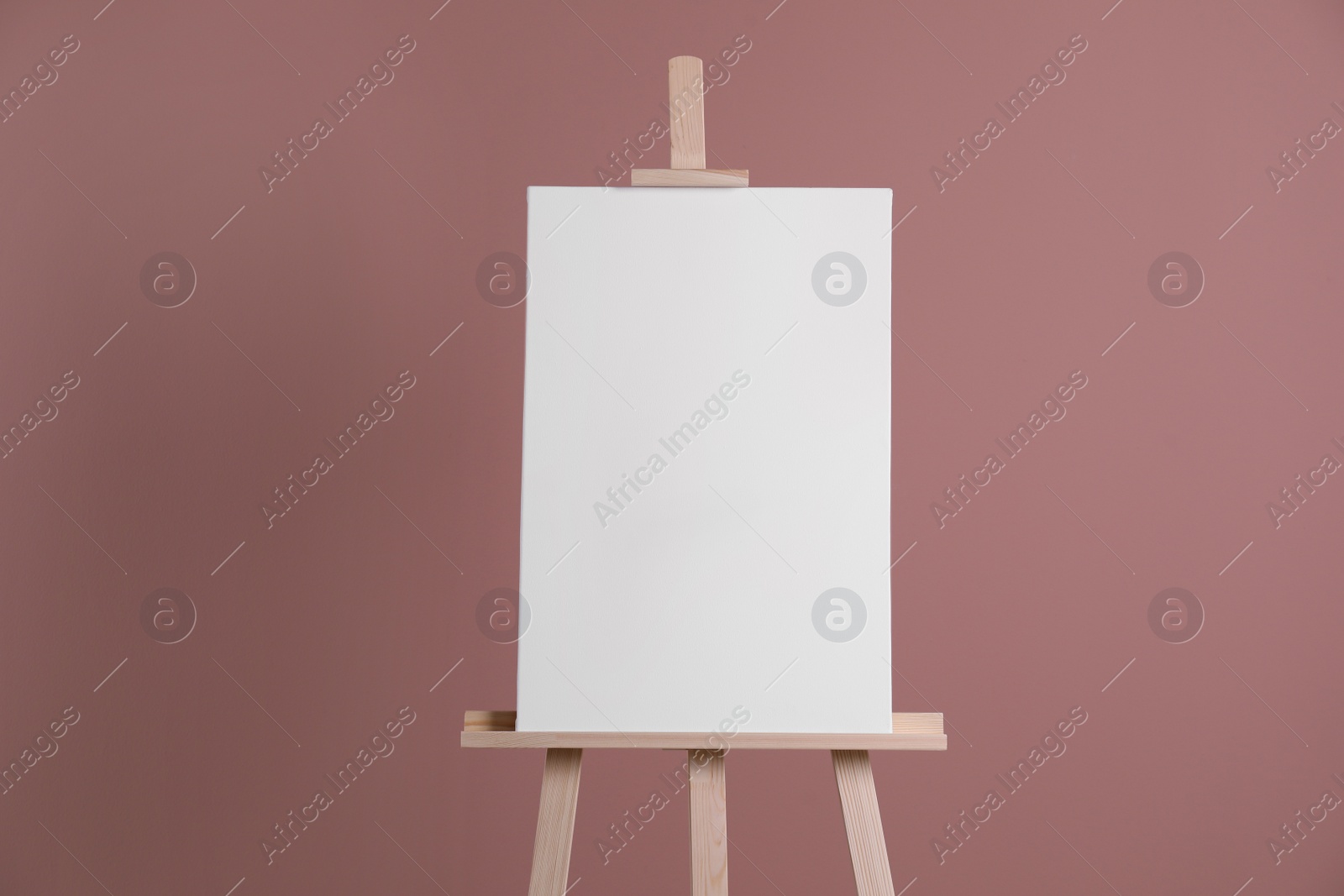 Photo of Wooden easel with blank canvas on dusty rose background