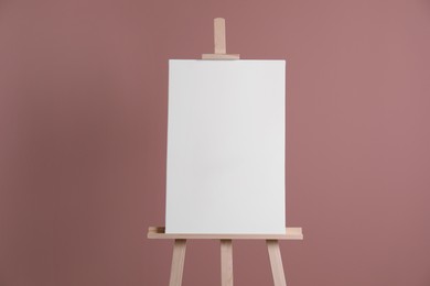 Photo of Wooden easel with blank canvas on dusty rose background