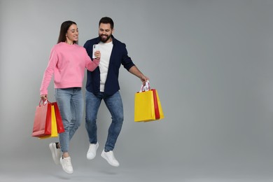 Photo of Happy couple with shopping bags and smartphone jumping on grey background. Space for text