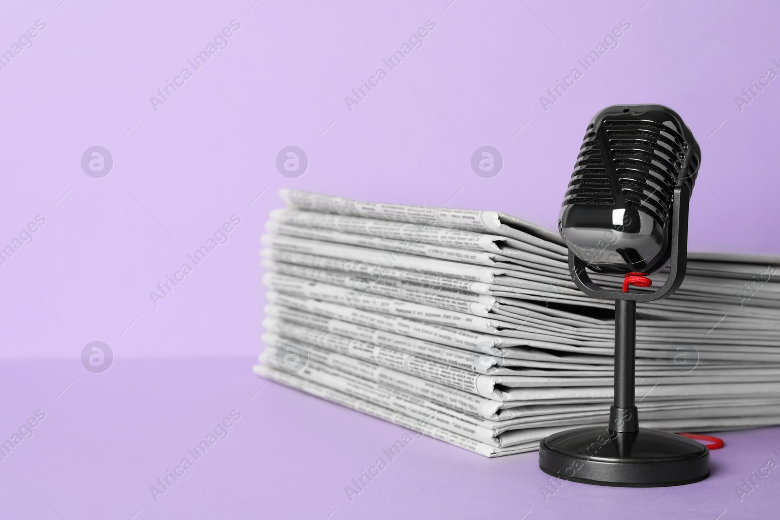 Photo of Newspapers and vintage microphone on light violet background, space for text. Journalist's work