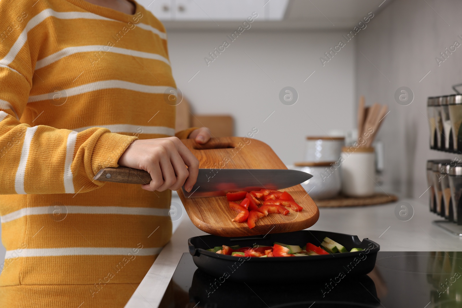 Photo of Cooking process. Woman adding cut bell pepper into pan with vegetables in kitchen, closeup