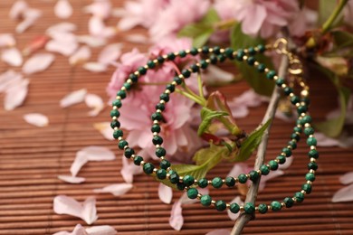 Photo of Beautiful blossoming branch, earrings and flower petals on bamboo mat, closeup