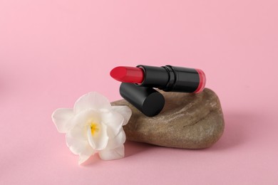 Photo of Beautiful lipstick on stone and white flower against pink background