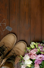 Military boots and flowers on wooden surface, space for text. Armed Forces Day