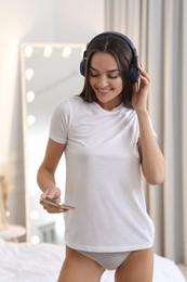 Photo of Young woman in white t-shirt and comfortable underwear listening to music indoors