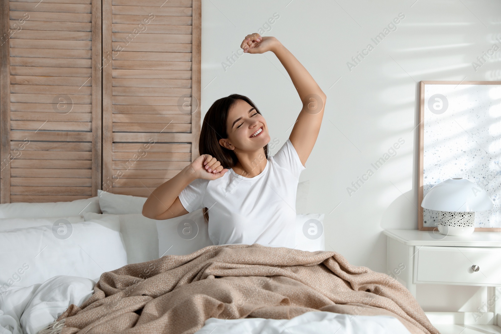 Photo of Woman covered with warm beige plaid stretching on bed indoors