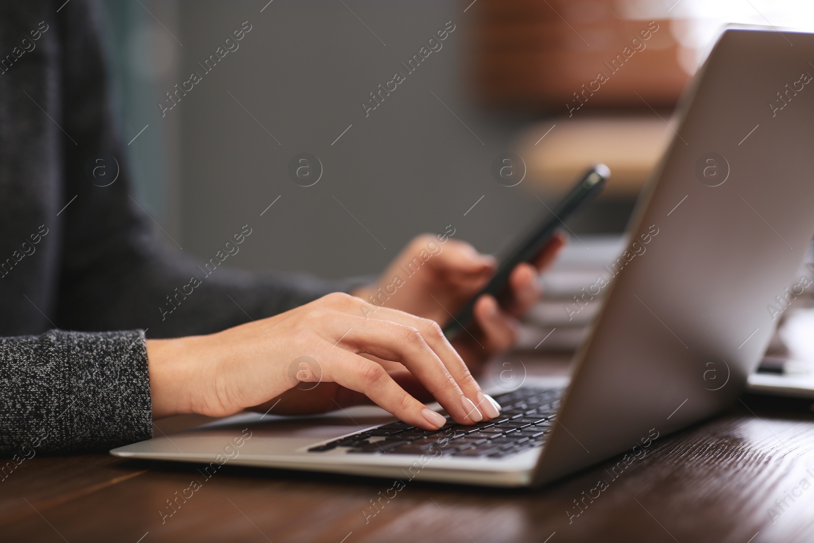 Photo of Woman with mobile phone working on modern laptop at table, closeup