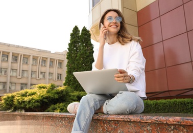 Image of Happy young woman with laptop talking on phone outdoors