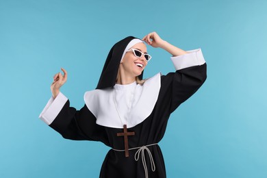 Happy woman in nun habit and sunglasses against light blue background