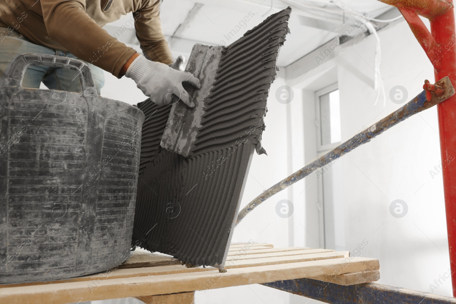 Photo of Worker applying cement on tile for installation in room, closeup